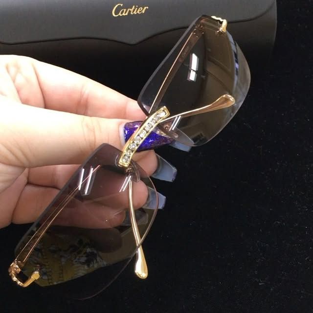 Hand holding gold-framed Cartier sunglasses with dark lenses and a blue gem accent on the temples