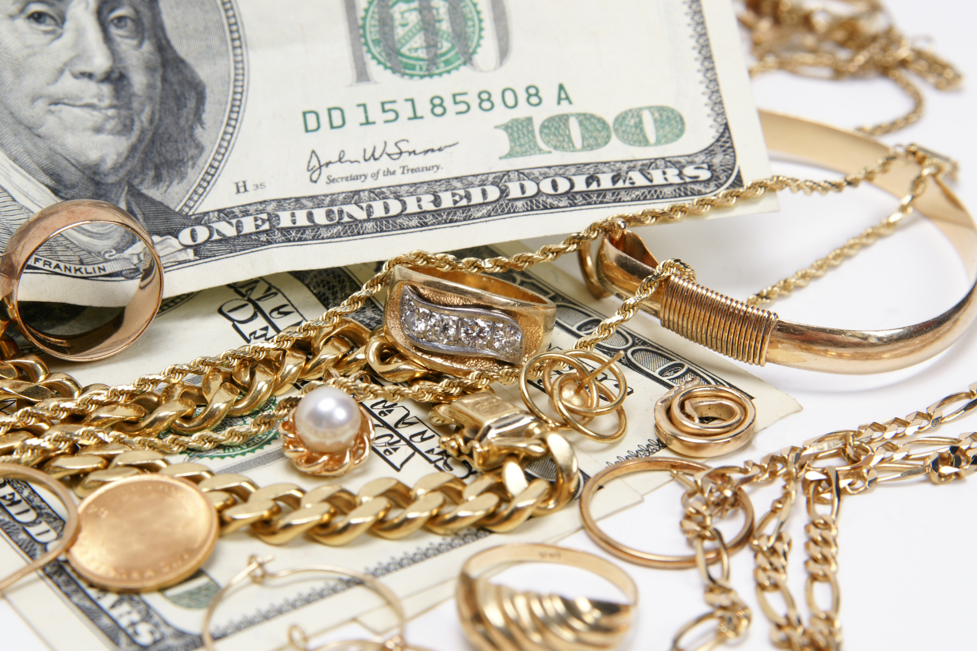 Gold jewelry and a U.S. hundred-dollar bill on a white surface