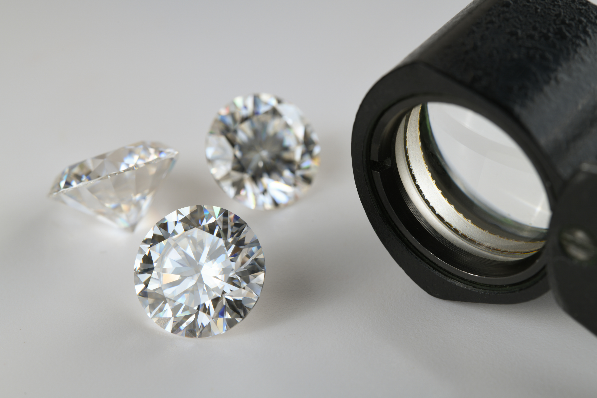 Loose diamonds beside a jeweler’s loupe on a light gray surface
