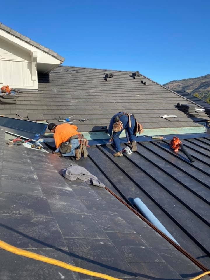 Two construction workers in high-visibility gear installing new metal roofing on a residential house.