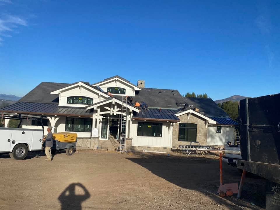 A partially constructed light-colored home under a clear blue sky, with a worker and a truck on the dirt front lot.