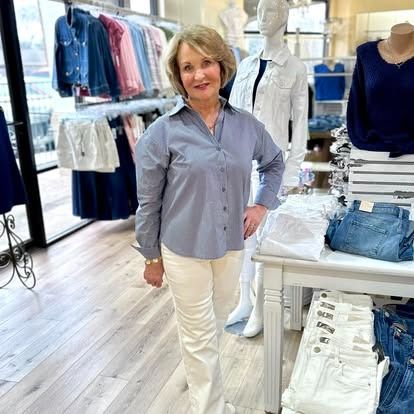 A woman in a blue shirt and white pants is standing in a clothing store.