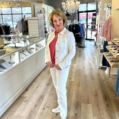 A woman in a white denim jacket and white pants is standing in a clothing store.