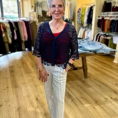 A woman is standing in a clothing store wearing a lace top and striped pants.