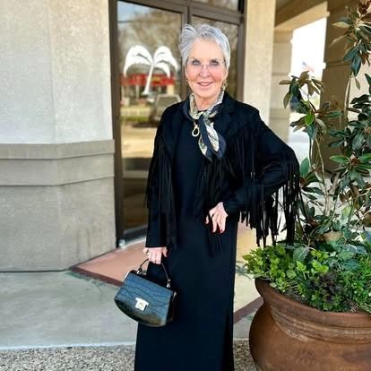 A woman in a black dress is standing next to a potted plant.