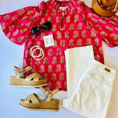 A pink shirt , white pants , sandals , sunglasses and a hat are on a table.