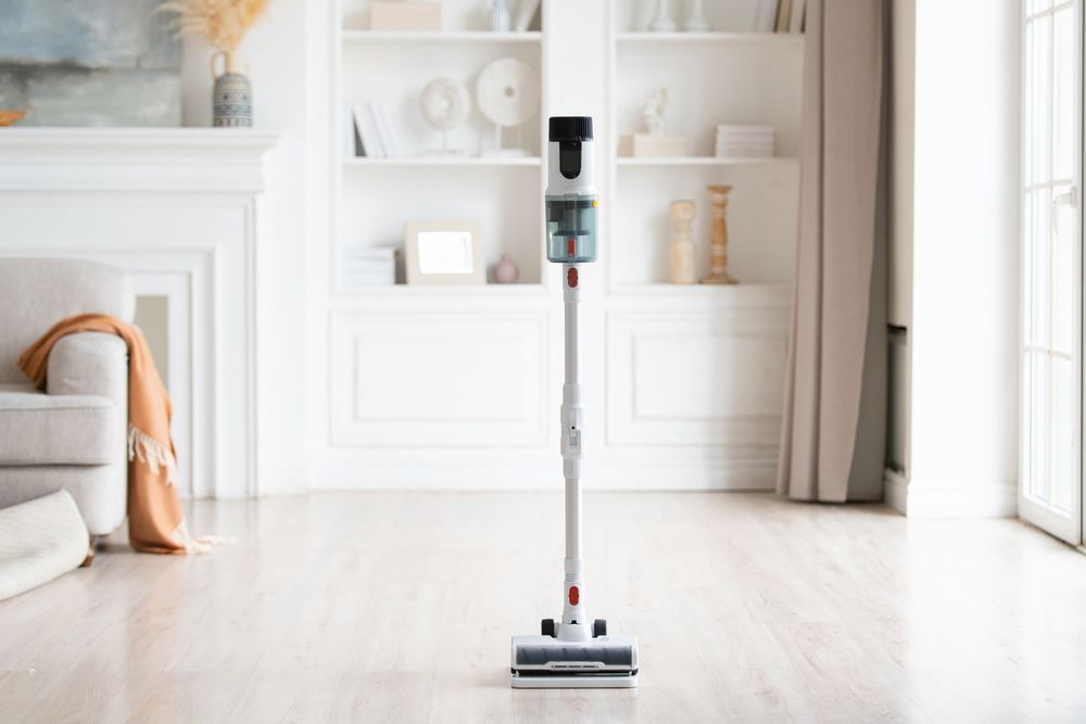 A Cordless Vacuum Cleaner Stands Upright on a Light-colored Floor — DAH Cleaning Services In Mareeba, QLD