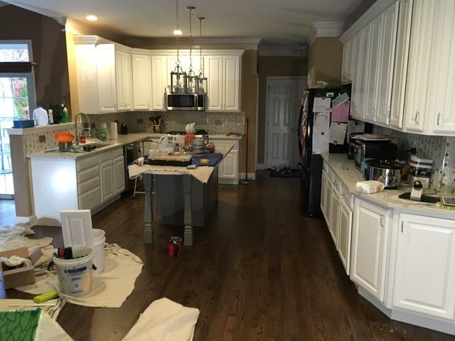 Kitchen with white cabinets, dark wood floors, and island; painting supplies on the floor.