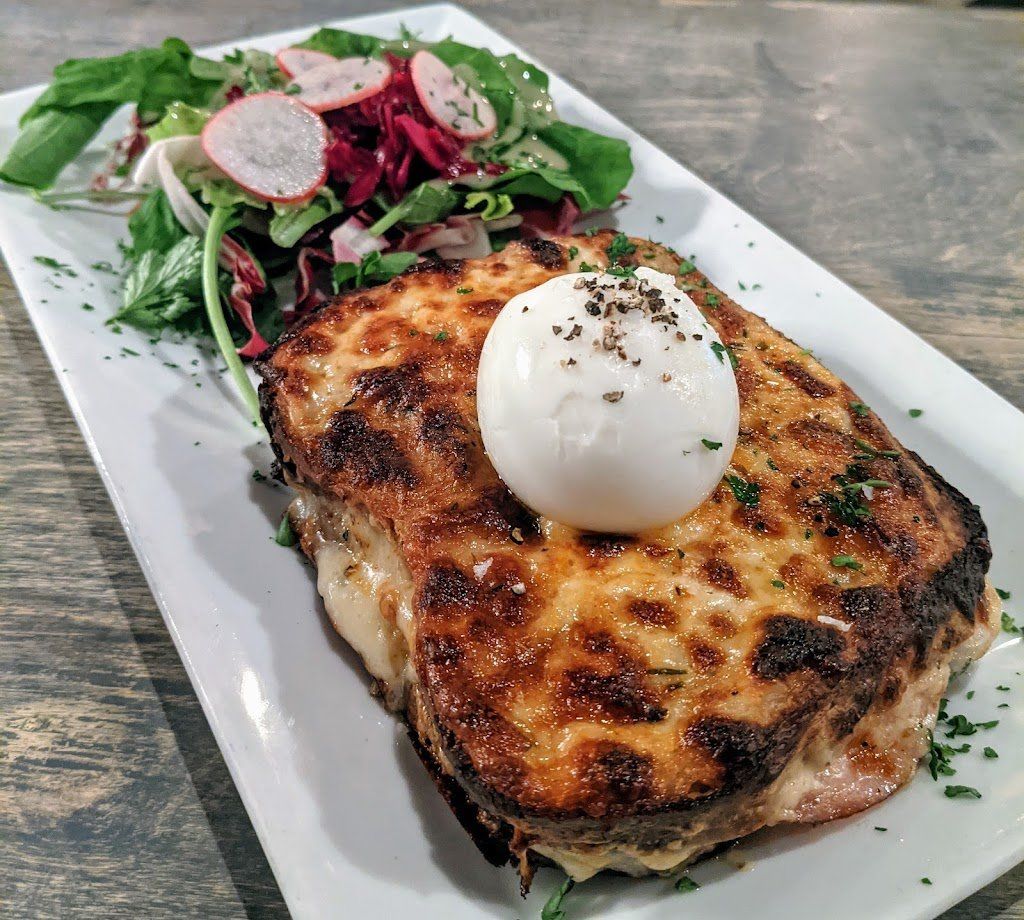 Croque madame sandwich with a poached egg and salad on a white plate.