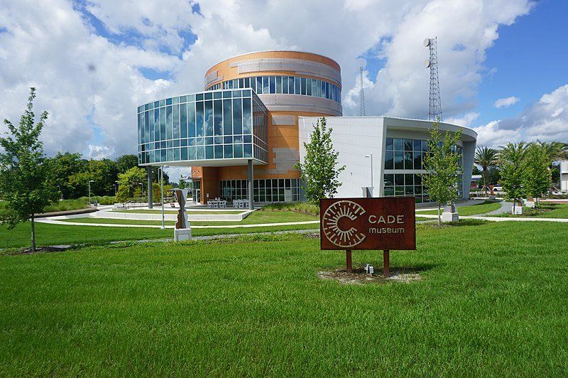 Modern building with curved glass and a cylindrical tower, grassy lawn with sign that reads 