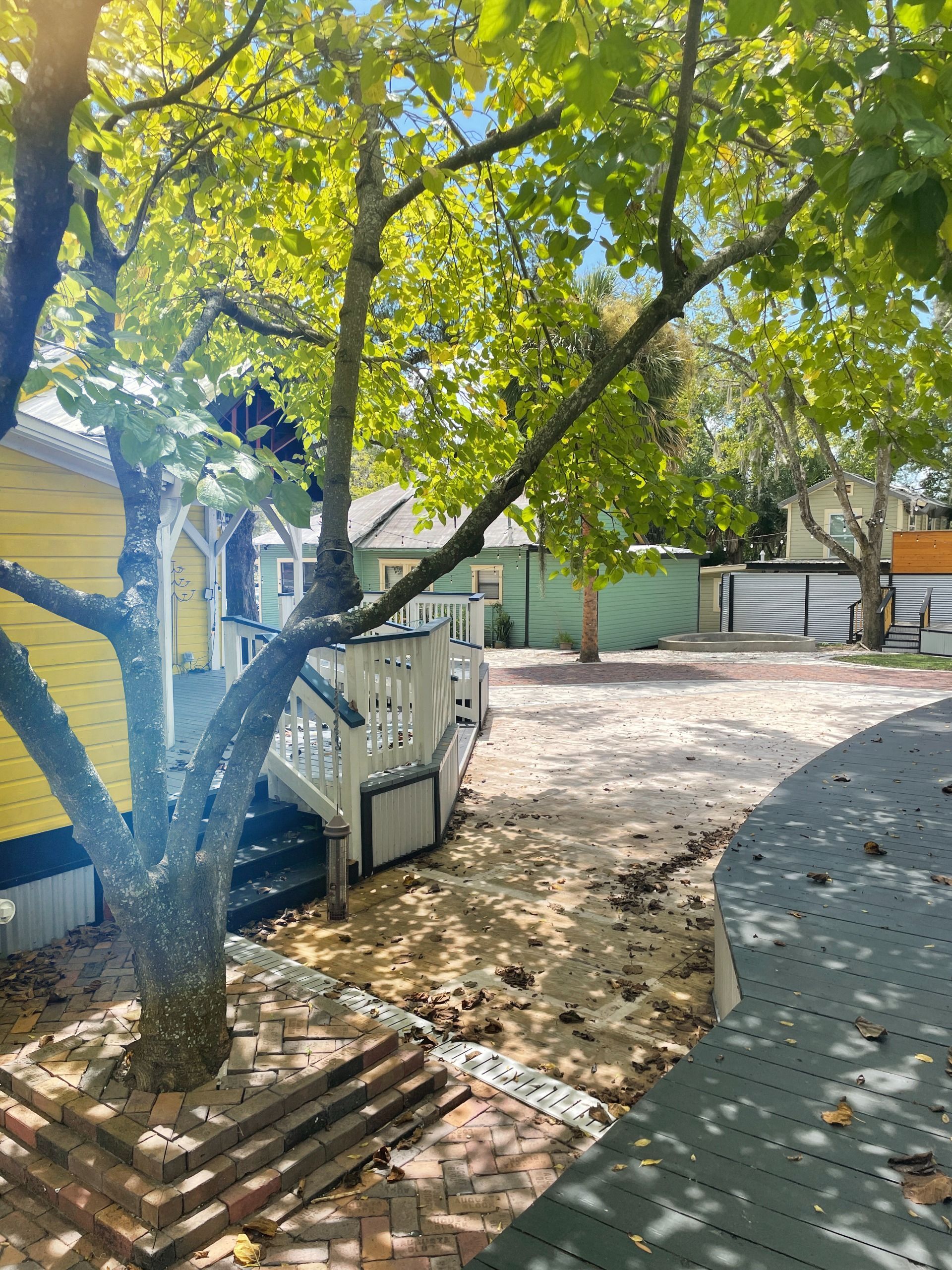 Yellow and white building with a porch, tree in foreground, gravel area. Sunny day.