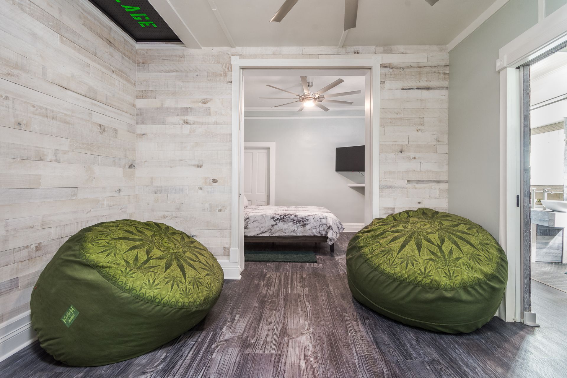 Two green beanbag chairs in a room with white wood paneling, leading to a bedroom.
