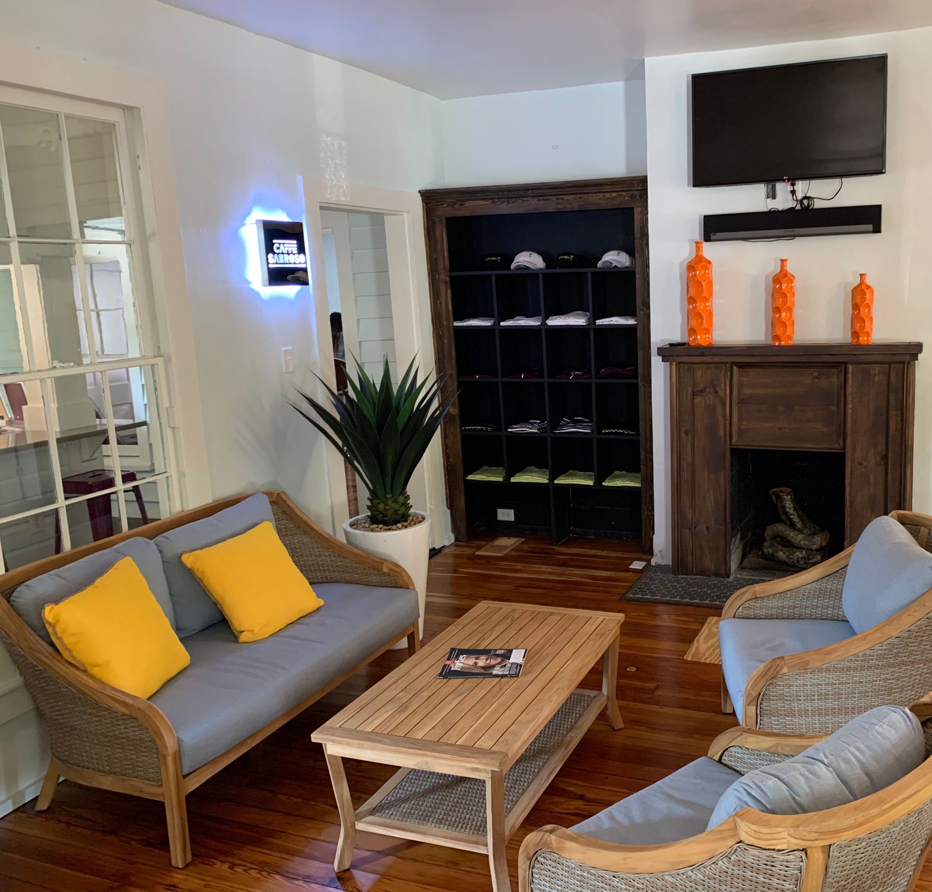 Cozy waiting room with wicker furniture, yellow cushions, and a fireplace. Wooden floor and storage.