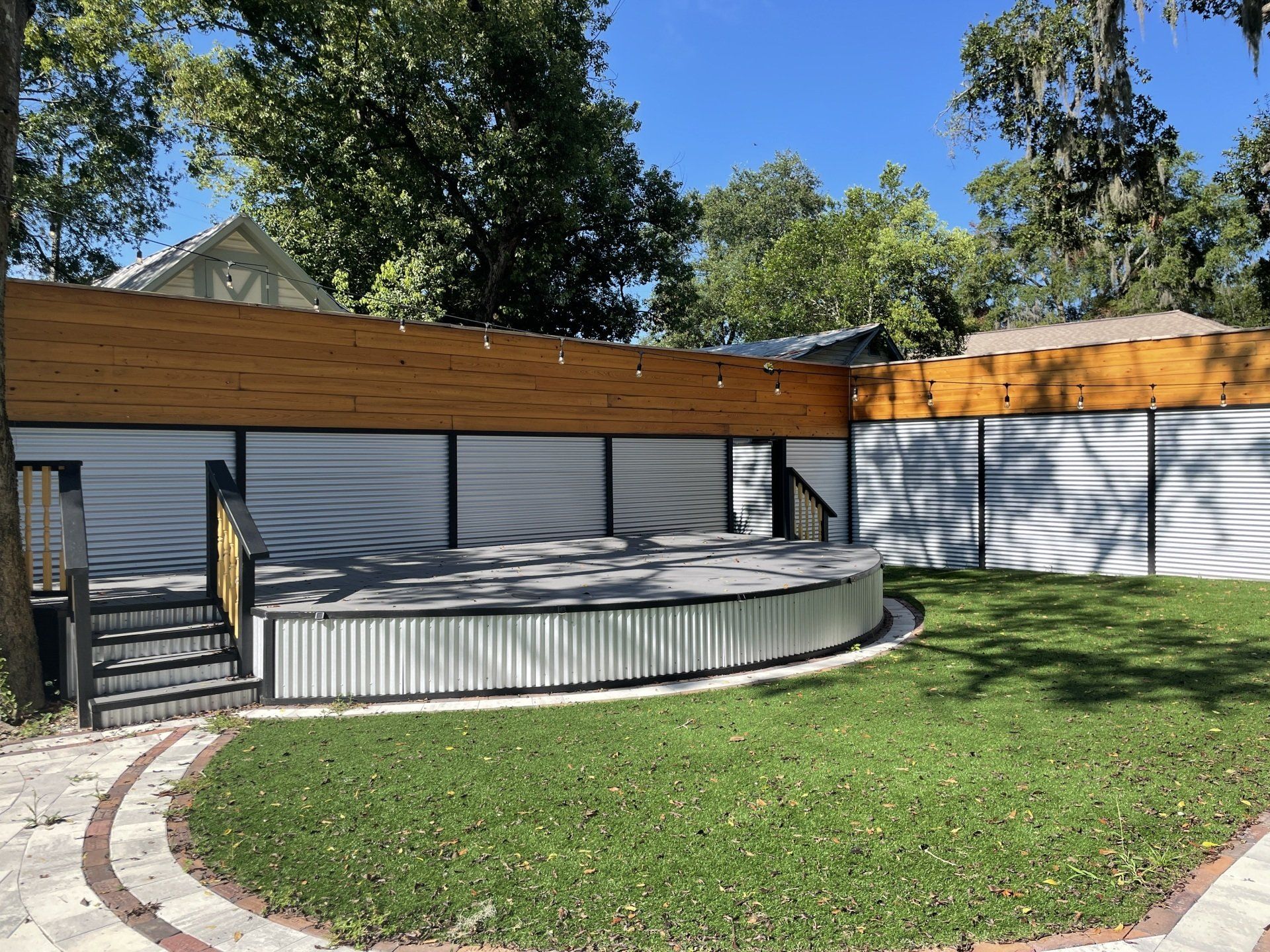 Outdoor stage with corrugated metal base, wooden trim, and green lawn.