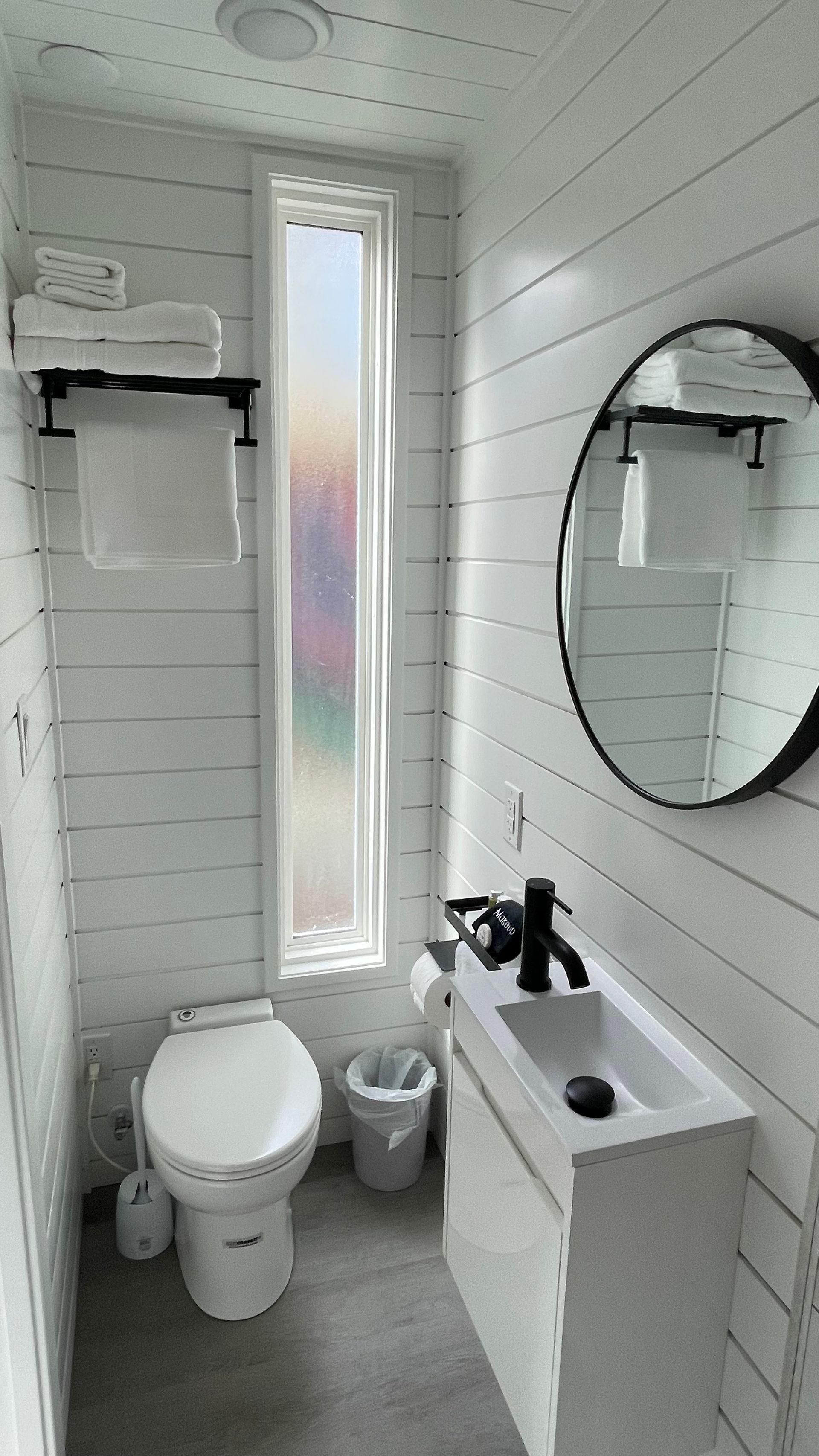 Small, modern bathroom with white shiplap walls, a toilet, sink, mirror, and towel rack.