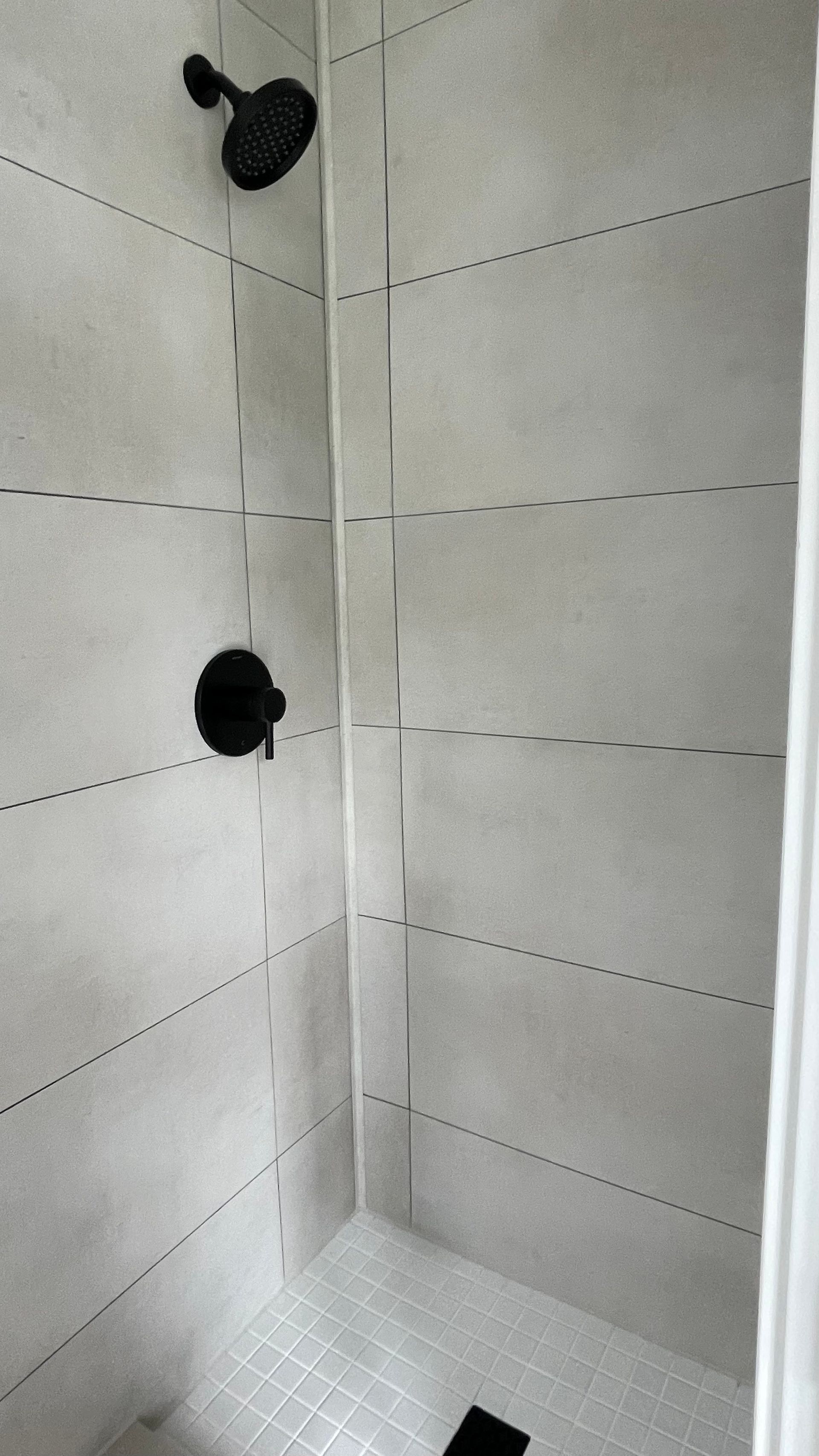 Black shower fixtures in a tiled shower with white and gray tiles.