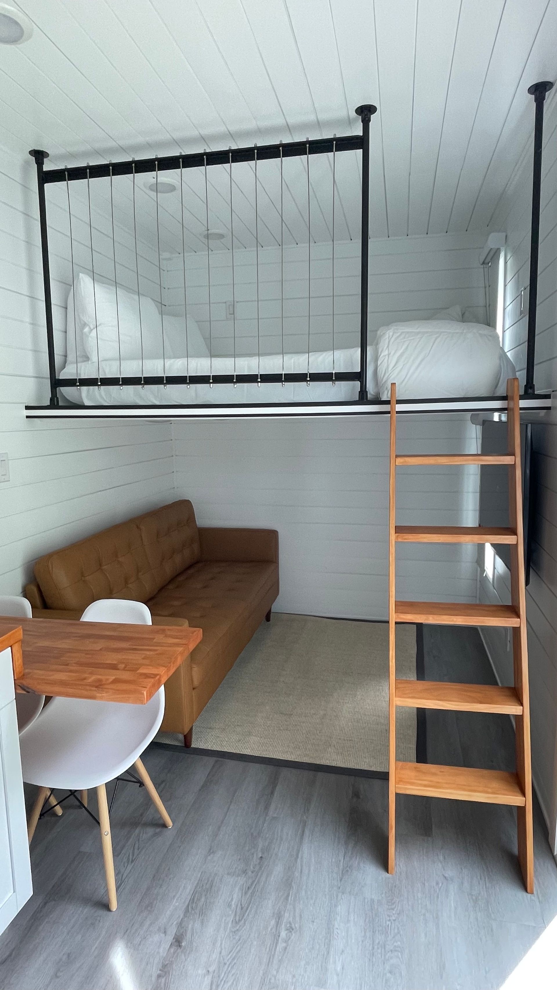 Interior of a tiny house with a loft bed, sofa, table, and wooden ladder.