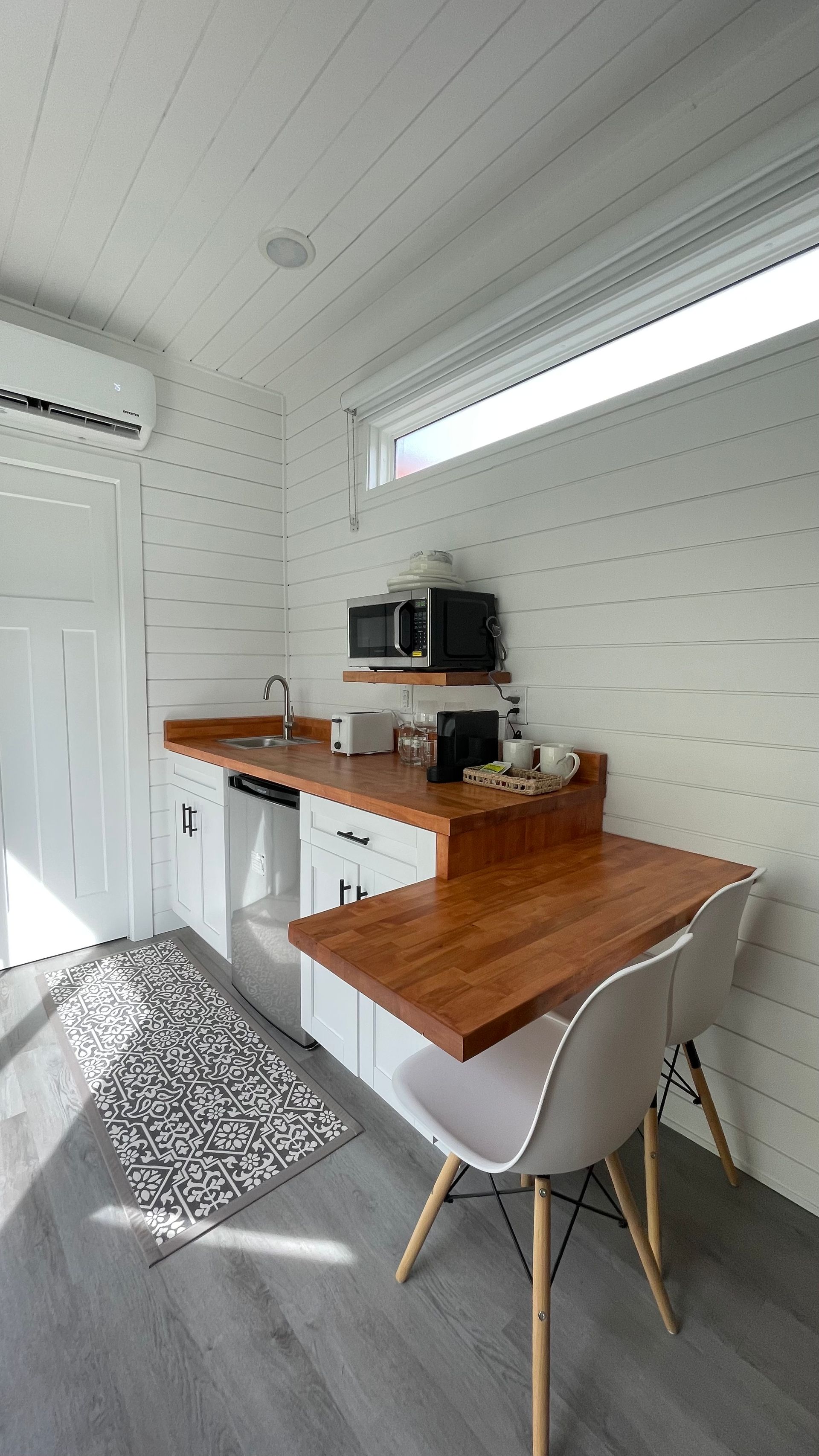 Compact white kitchen with wood countertops and a fold-out table, two chairs, and a small rug.