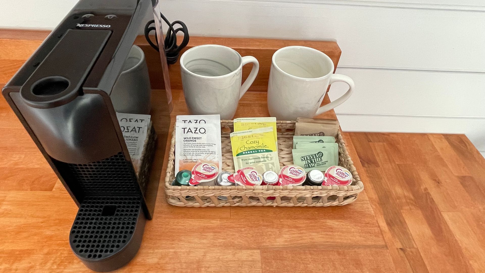 Coffee machine with mugs, tea bags, and pods on a wooden counter.