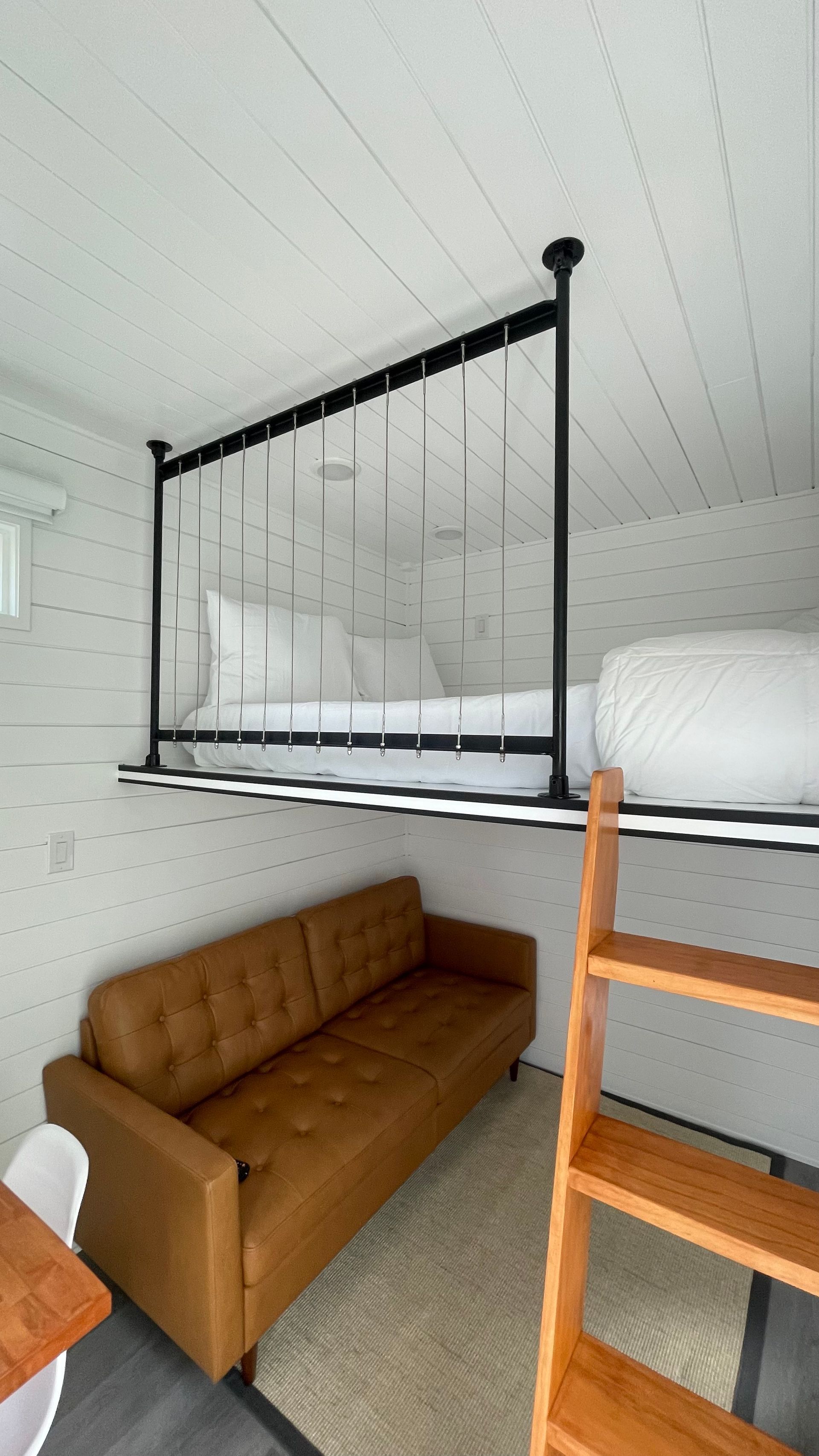 Loft bed above a brown sofa in a tiny house with a wooden ladder.