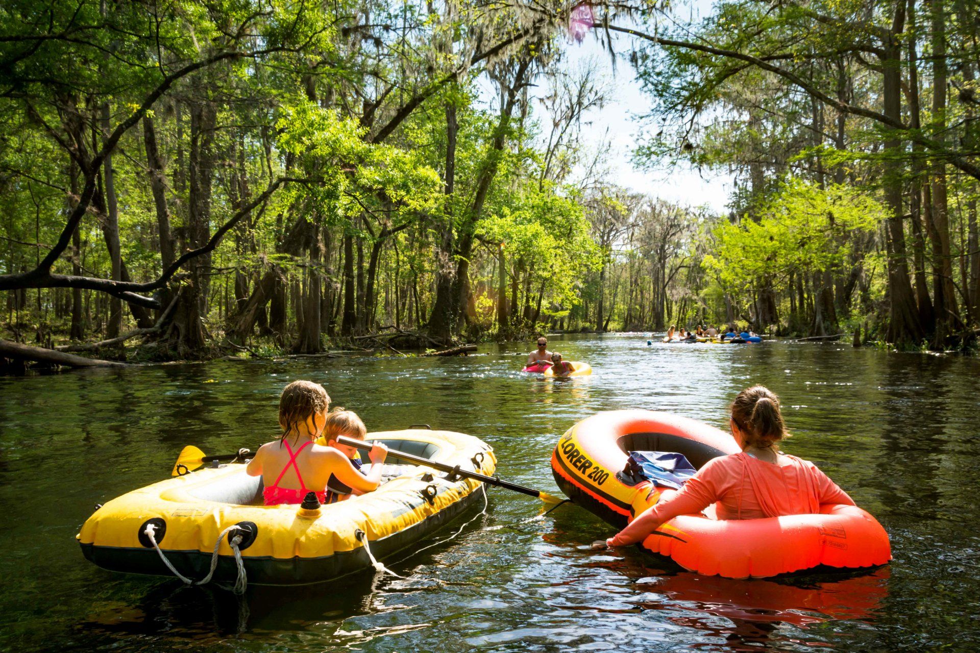 People tubing and boating on a river surrounded by trees.