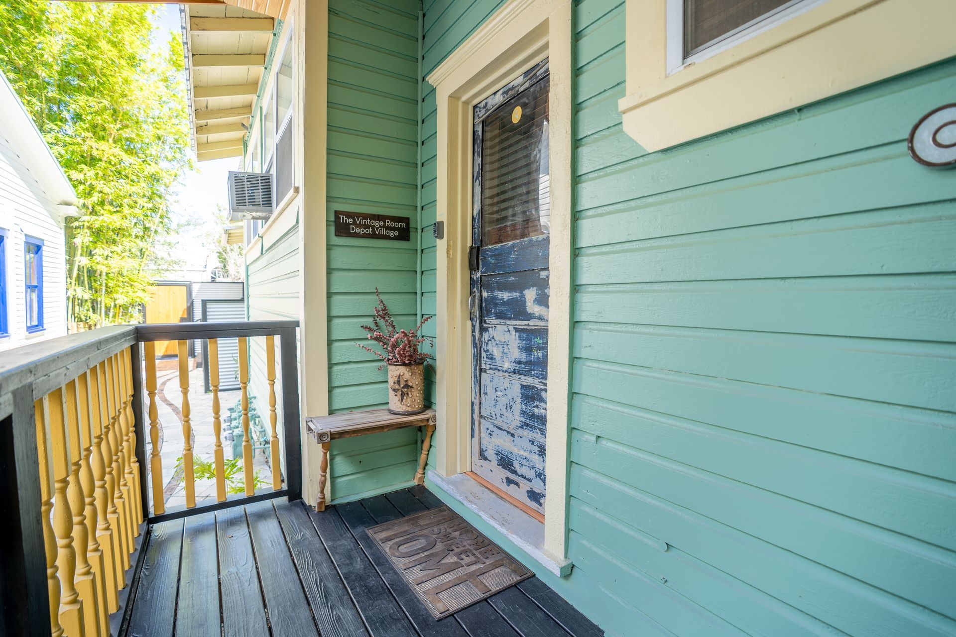Teal house exterior with a porch, black door, and yellow railing.