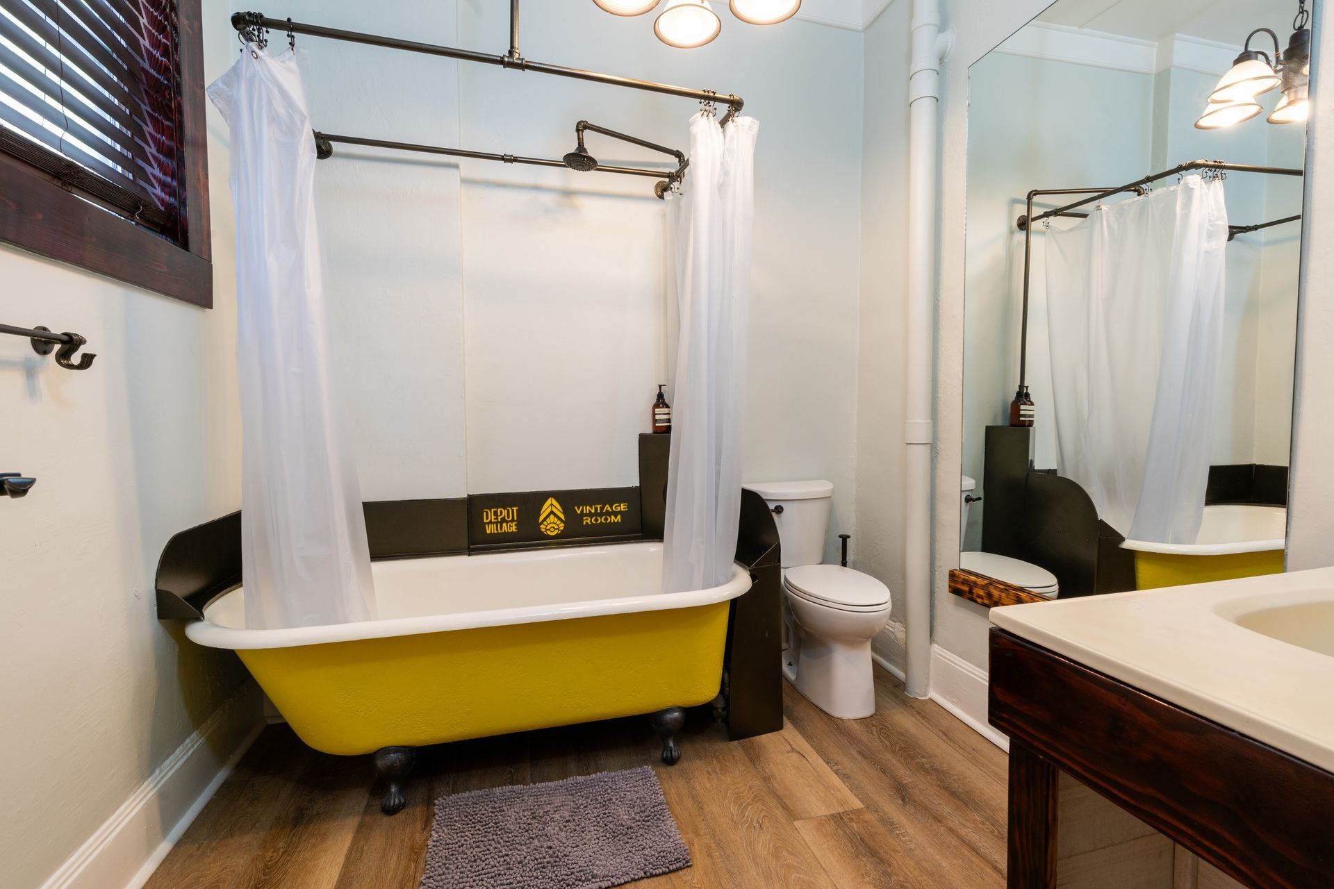 Yellow claw-foot bathtub with shower curtain in a bathroom, near a toilet and vanity.