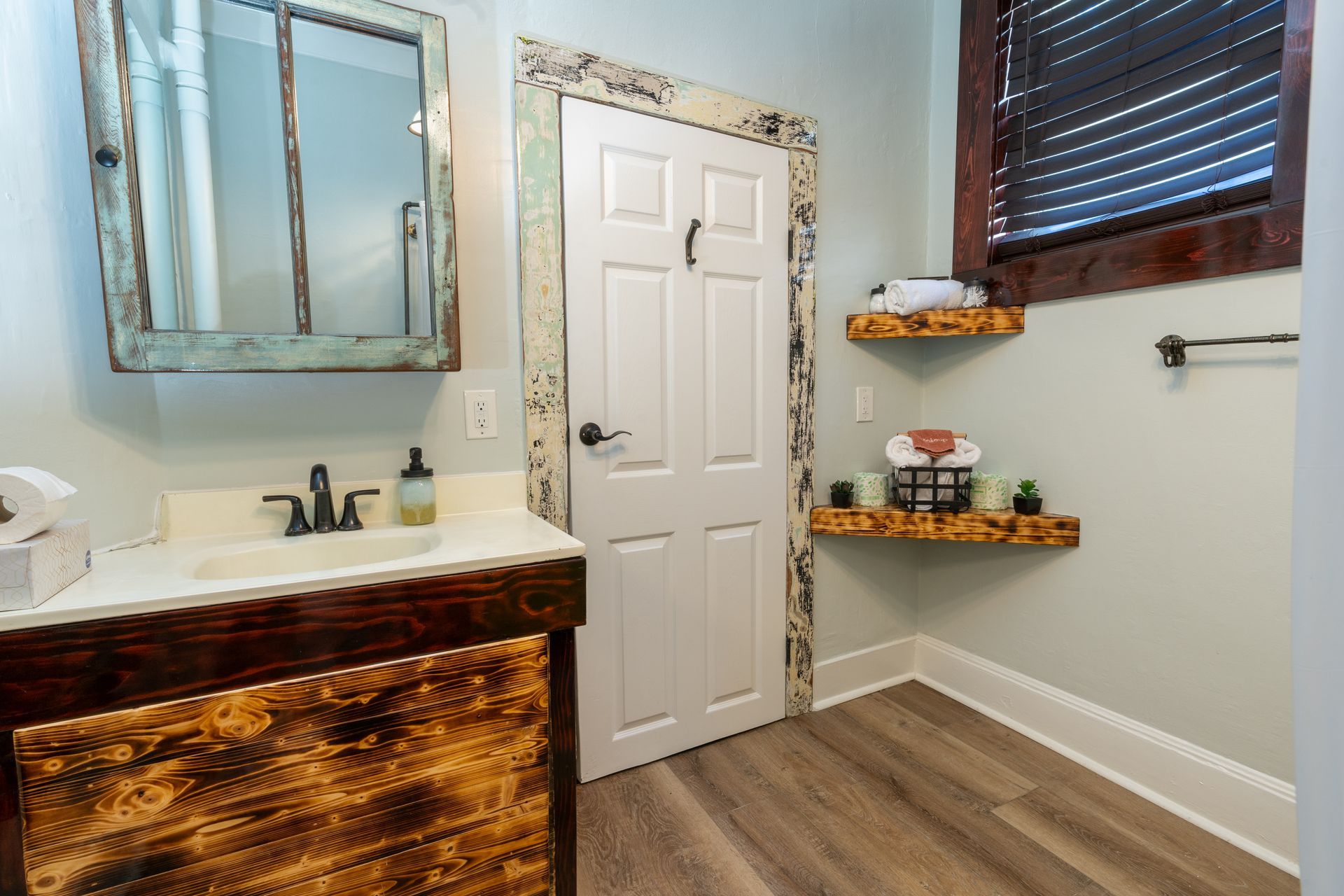 Rustic bathroom with wood vanity, shelves, and window frame, white door.