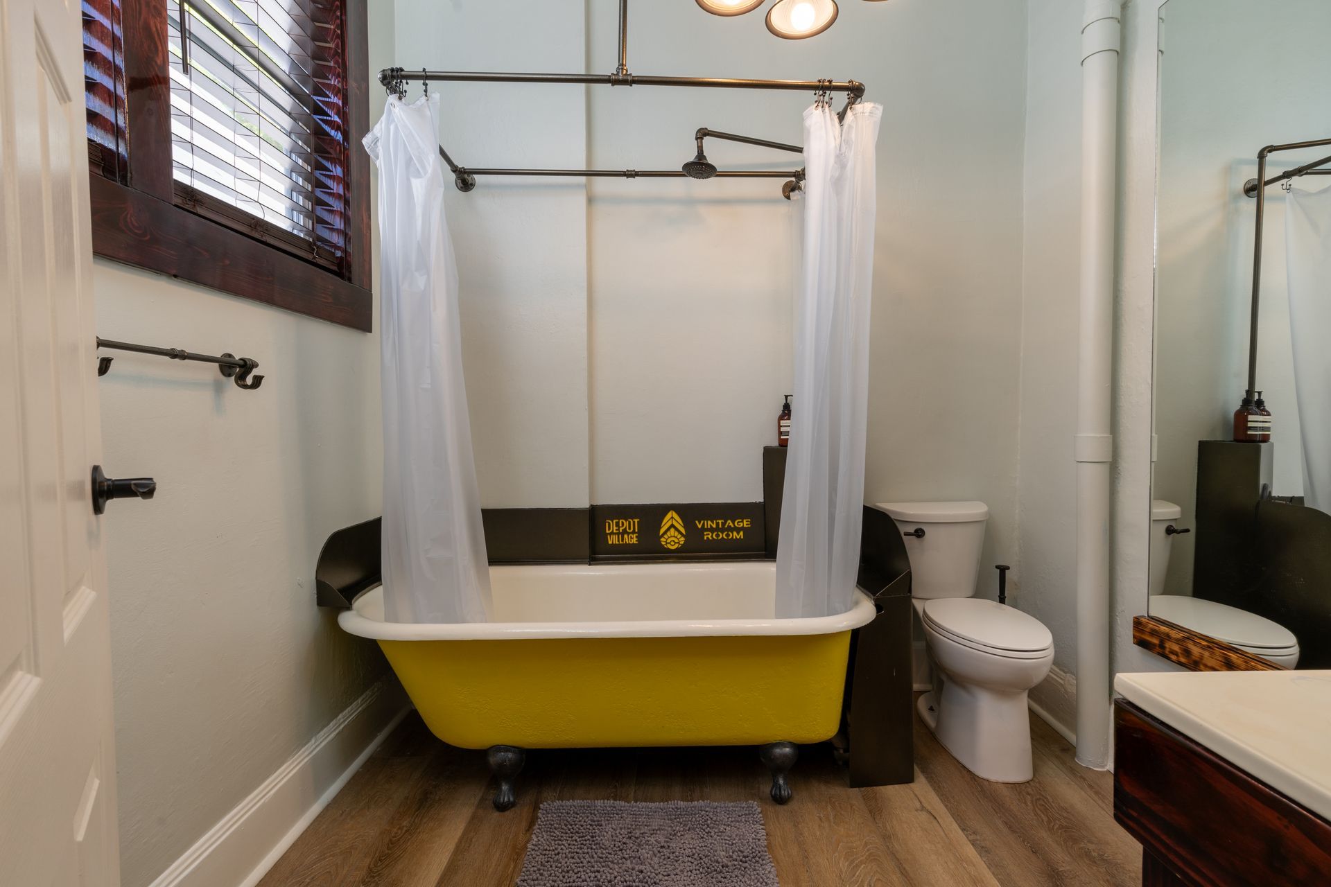 Yellow clawfoot bathtub with industrial pipe shower rod, white shower curtain, and toilet in a bathroom.
