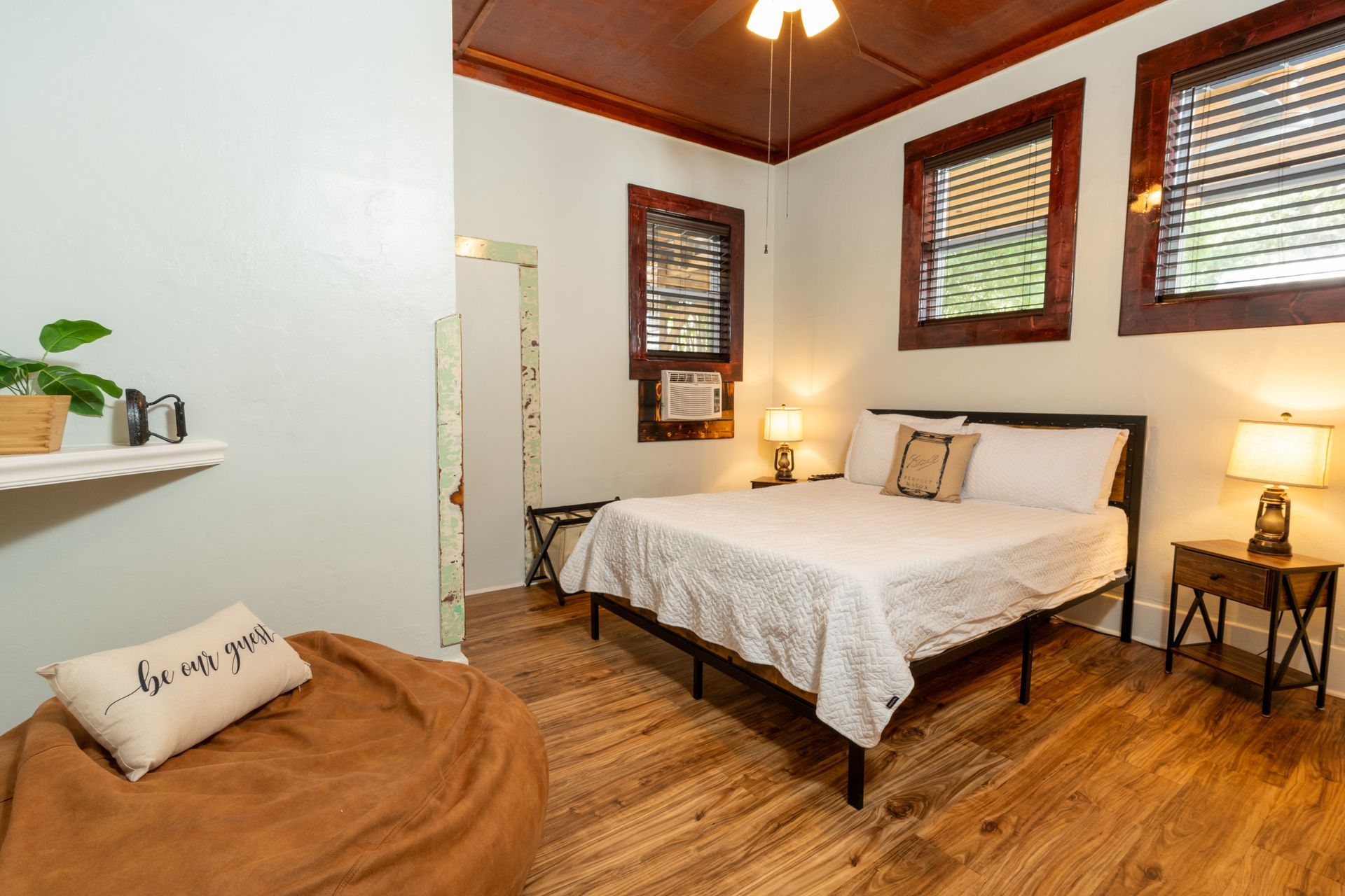 Bedroom with bed, beanbag chair, wooden floor and trim, windows.