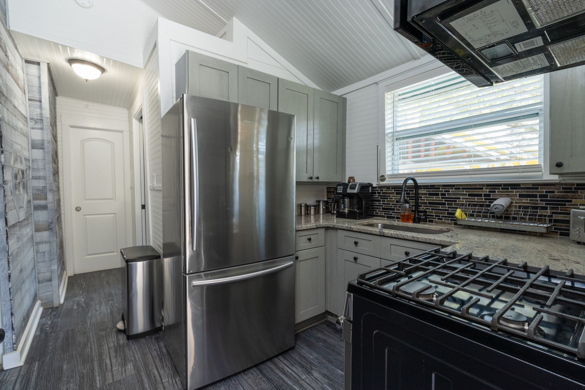 A small kitchen with gray cabinets, stainless steel fridge, stove, and a window.