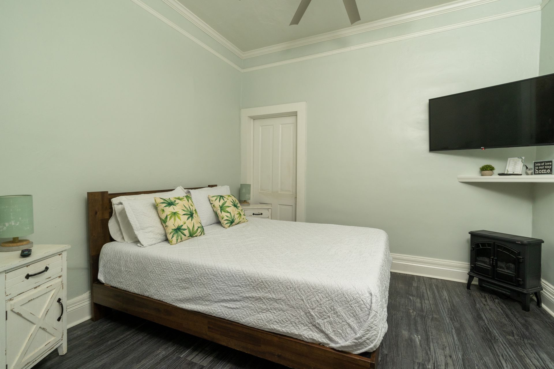 Bedroom with bed, TV, nightstand, and small fireplace against a light green wall.