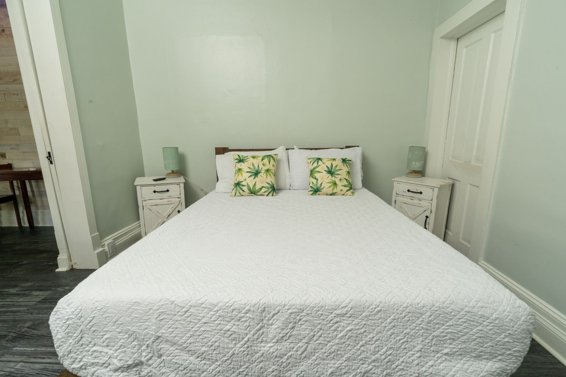 Bedroom with a white bed, bedside tables, and green walls. Two tropical-print pillows.