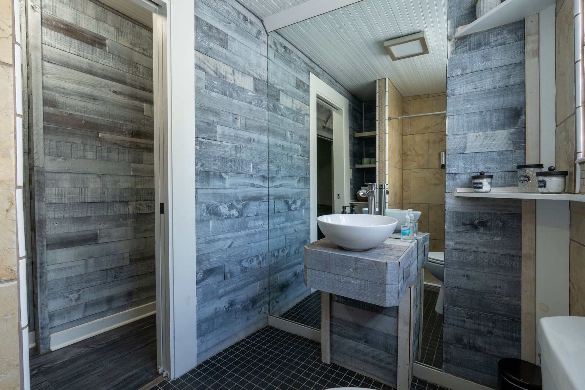 Bathroom with gray and white wood-like paneling, a white sink on a stone base, and black tile flooring.