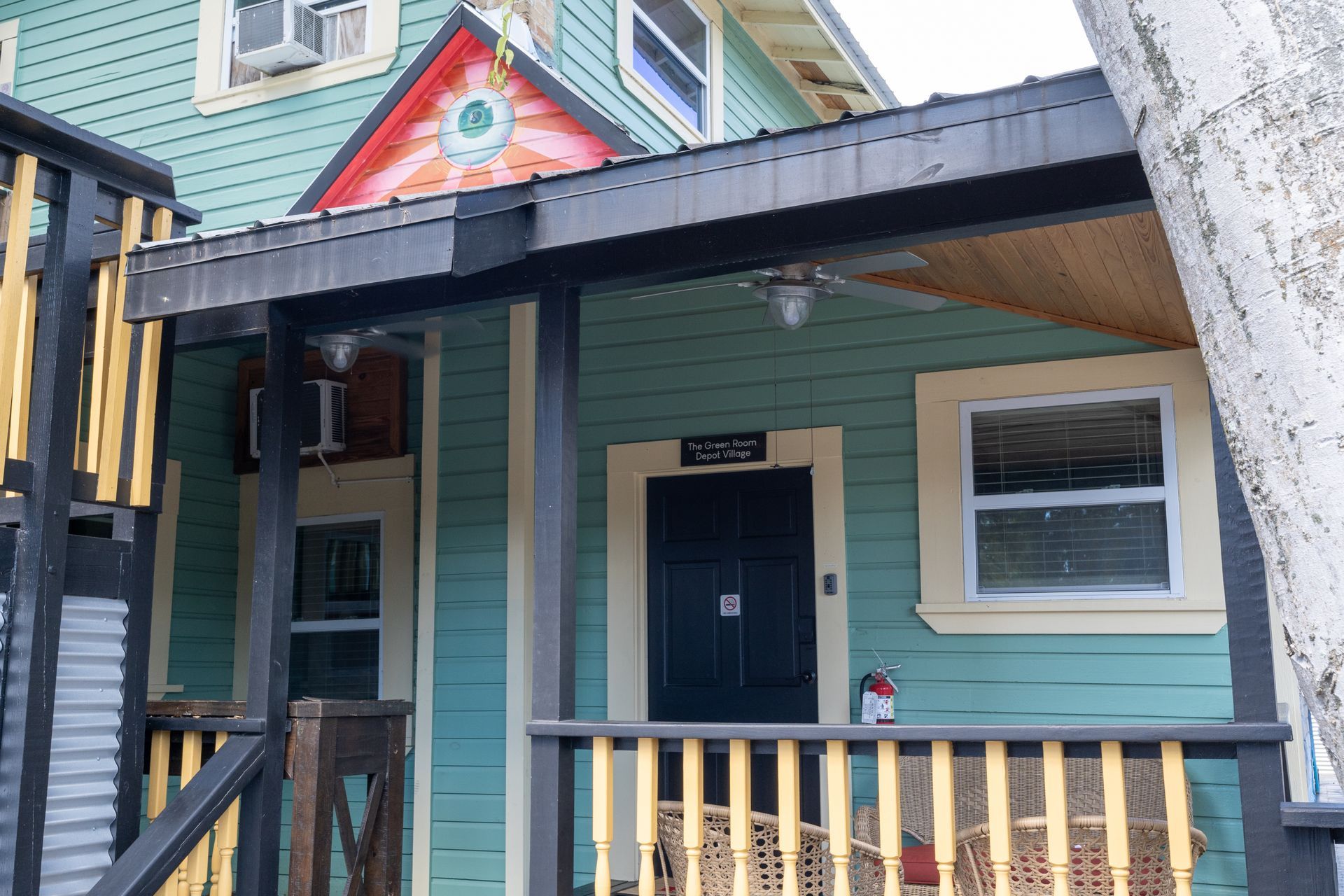 Turquoise house with porch, black door, and a red-and-gold mural on the roof.