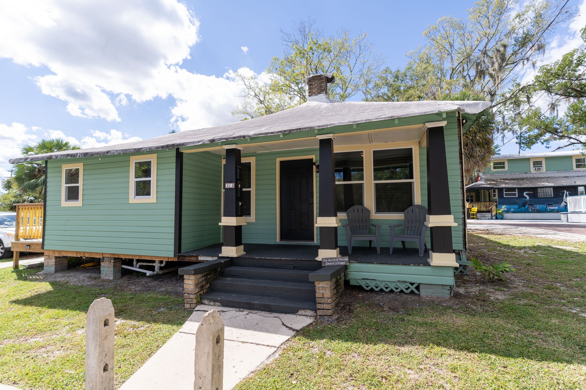 Green bungalow with a front porch and black accents.