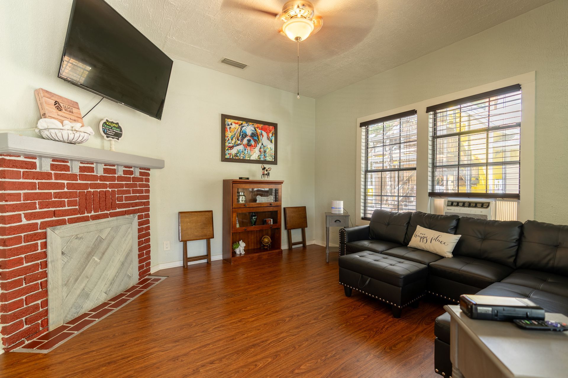 Living room with fireplace, leather sectional sofa, hardwood floors, and windows.