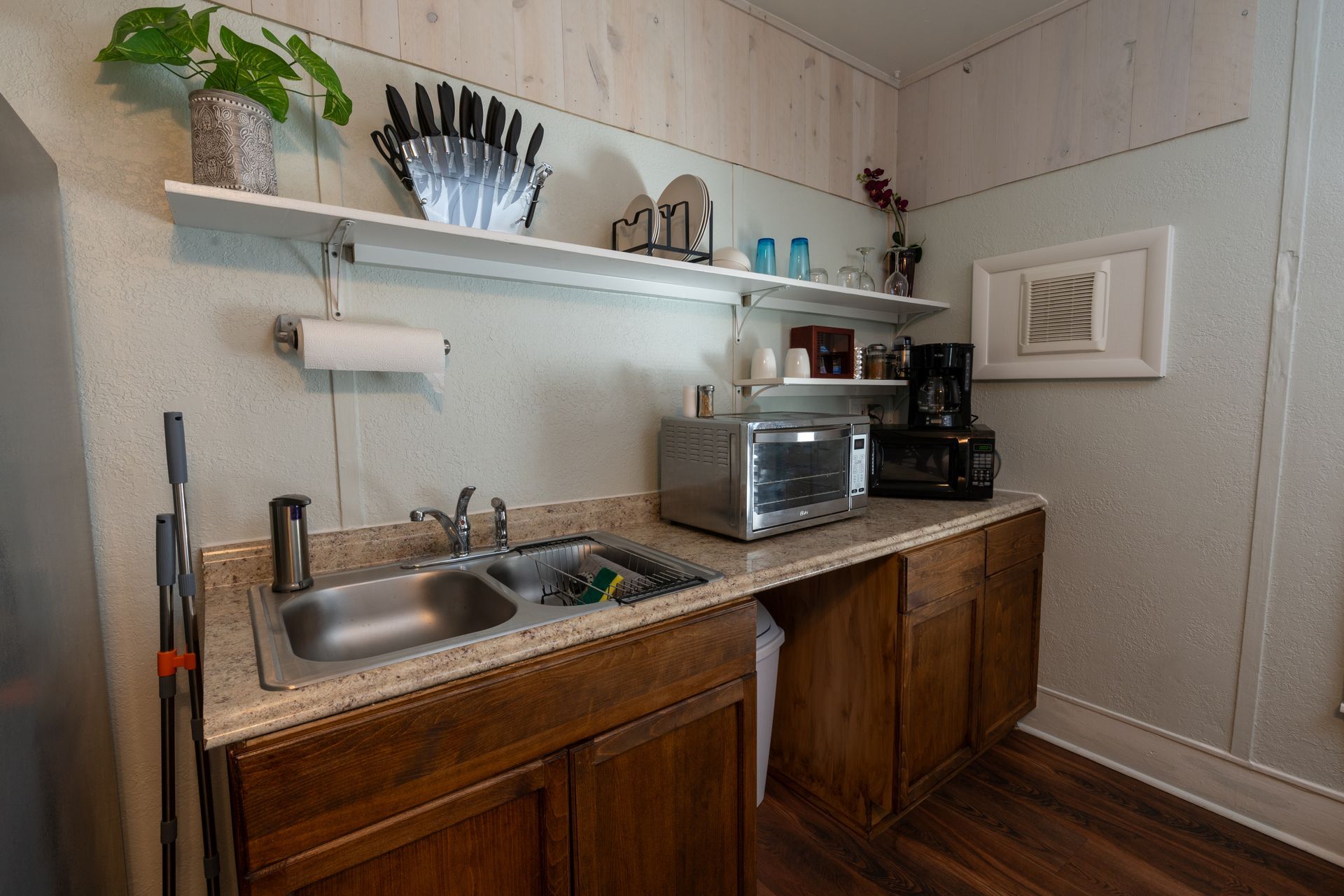 Small kitchen with sink, countertop, cabinets, toaster oven, coffee maker, shelves, and a paper towel holder.