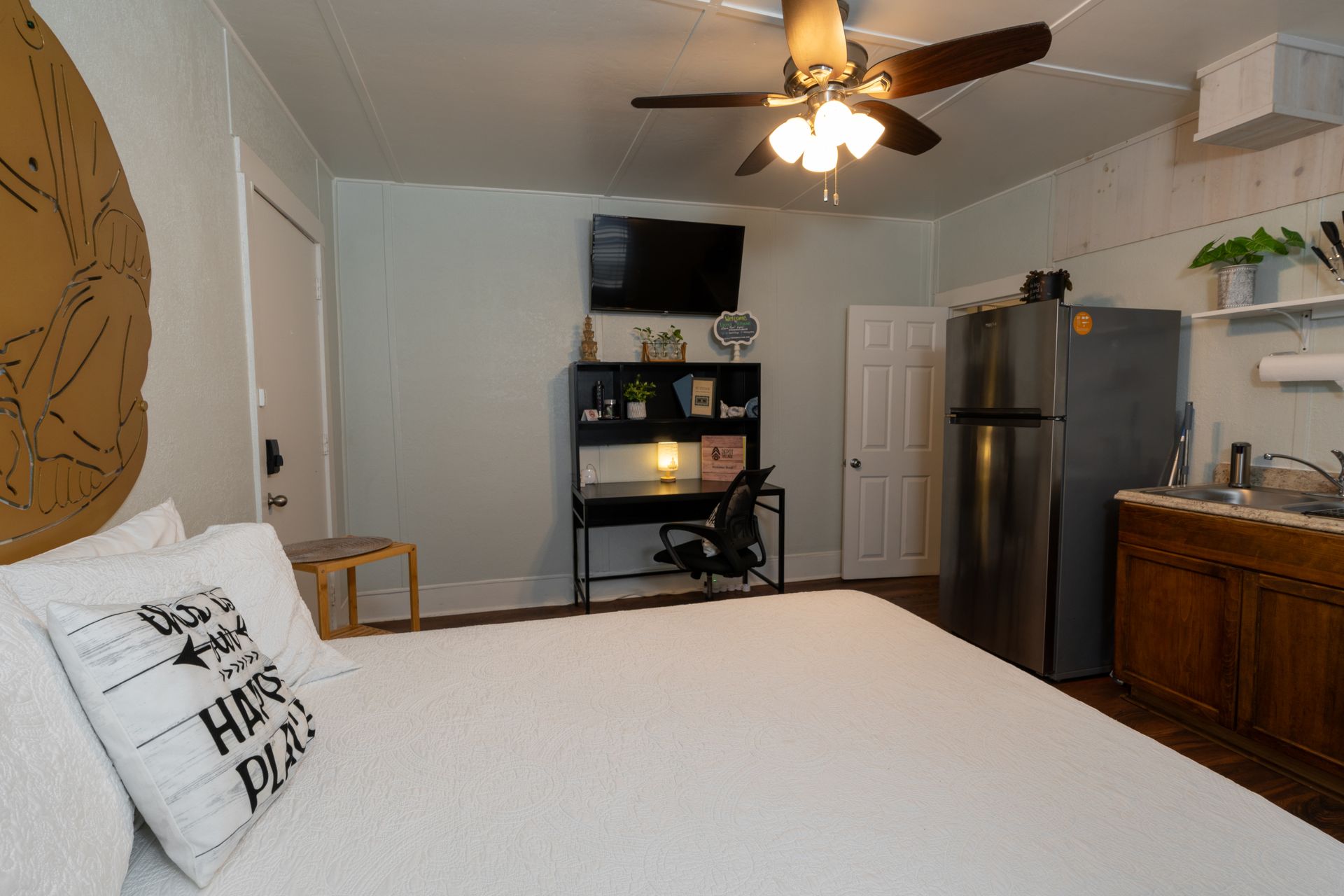 Small studio apartment with a bed, desk, kitchenette, and ceiling fan.