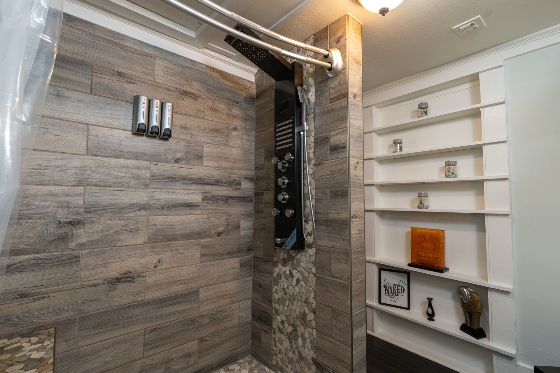 A modern shower with gray tile, shower panel, and built-in shelving.