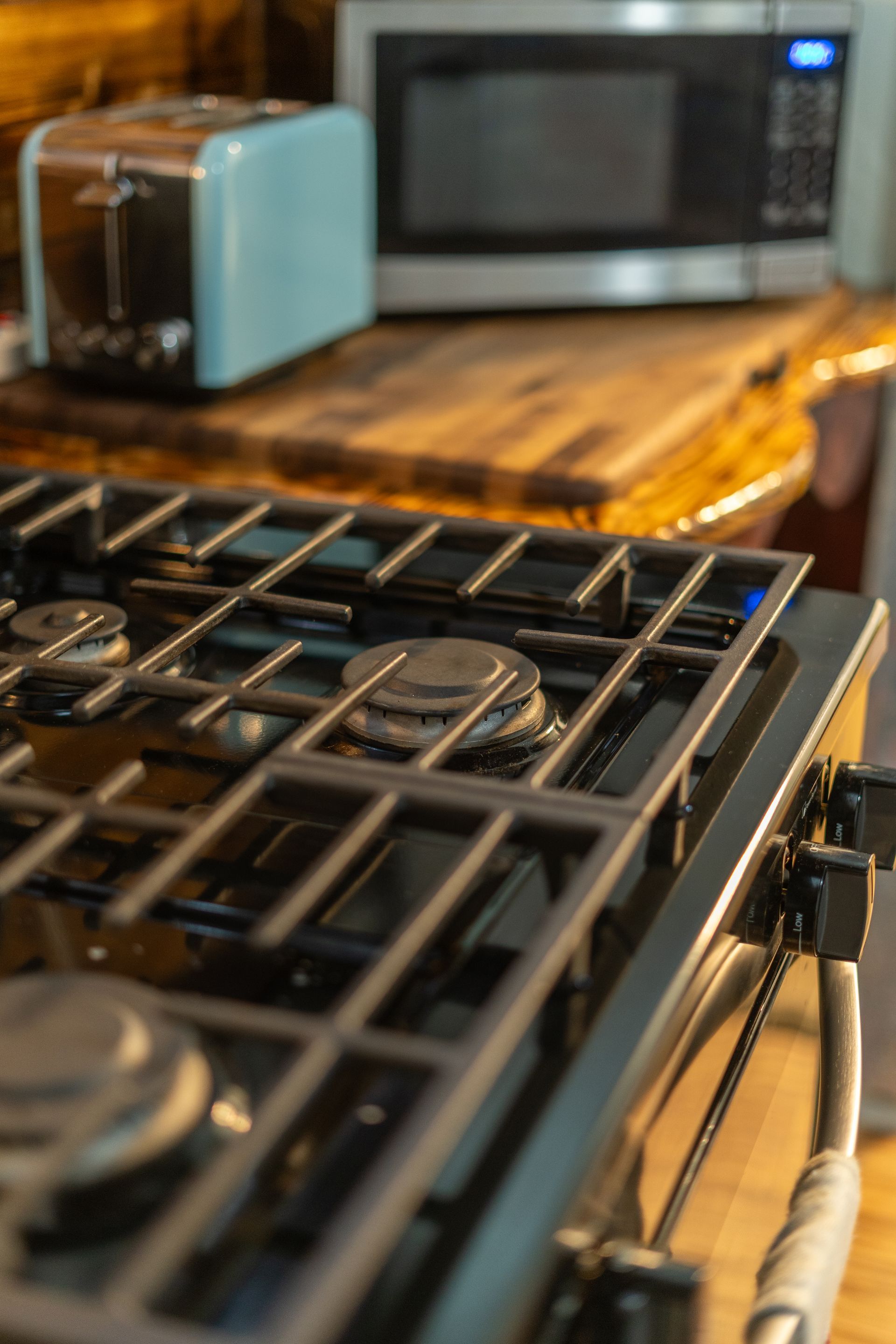 Gas stovetop with grates in focus, a toaster and microwave in the background.