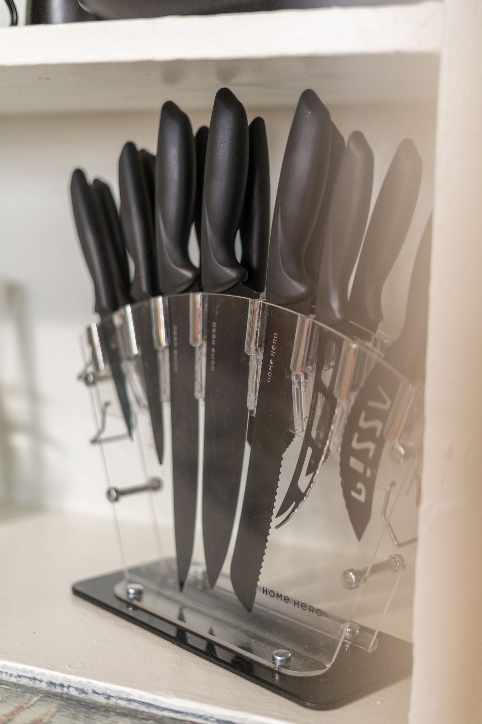Black-handled kitchen knives in a clear acrylic block stand inside a cabinet.