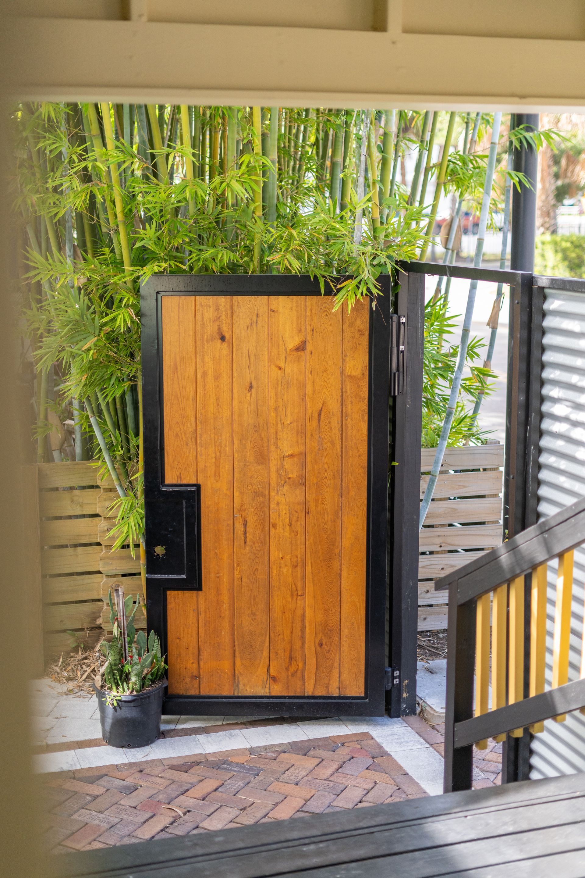 Wooden gate with black frame, next to fence and bamboo; potted plant on left.
