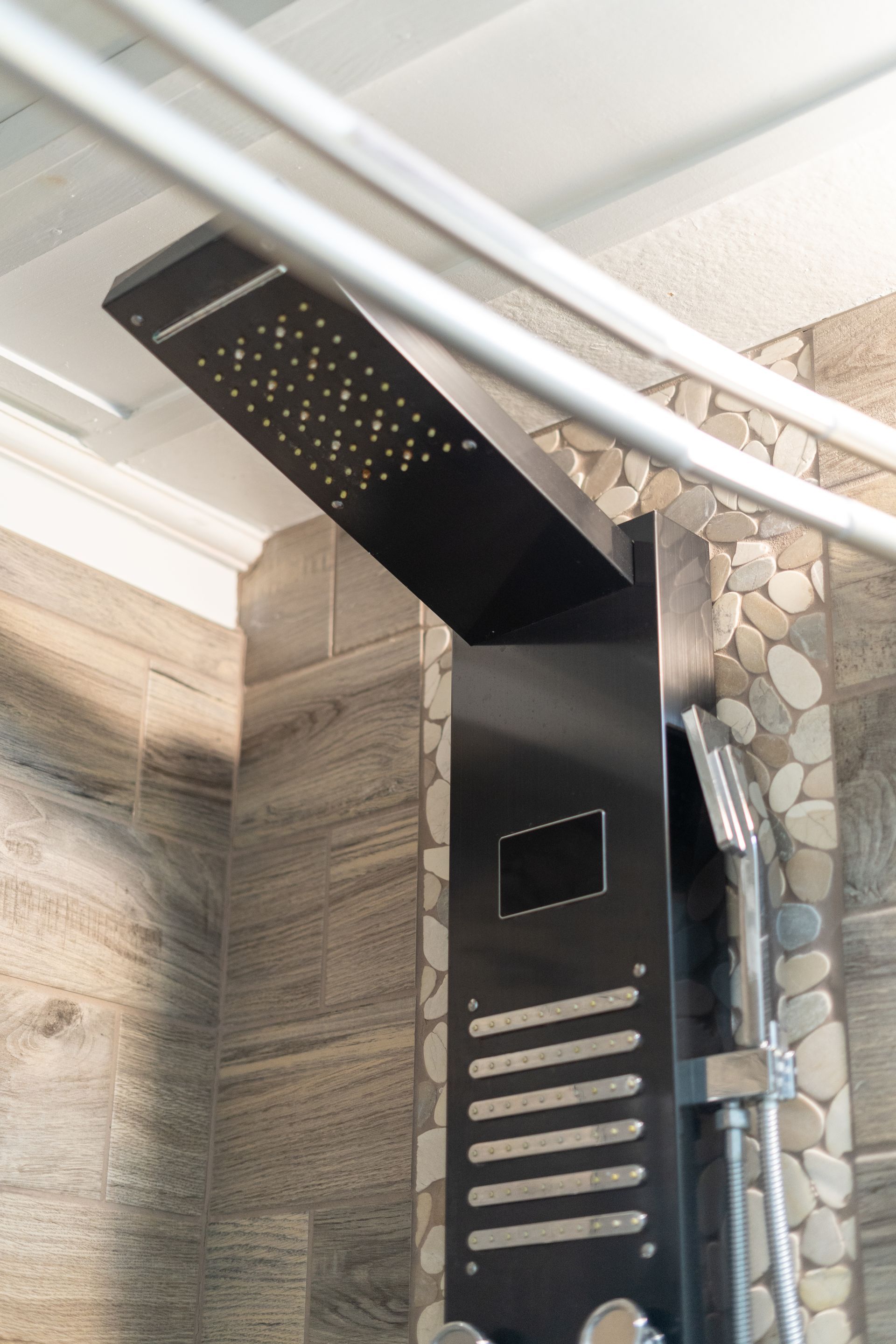Black shower panel with rain shower head, hand shower, and pebble tile wall.