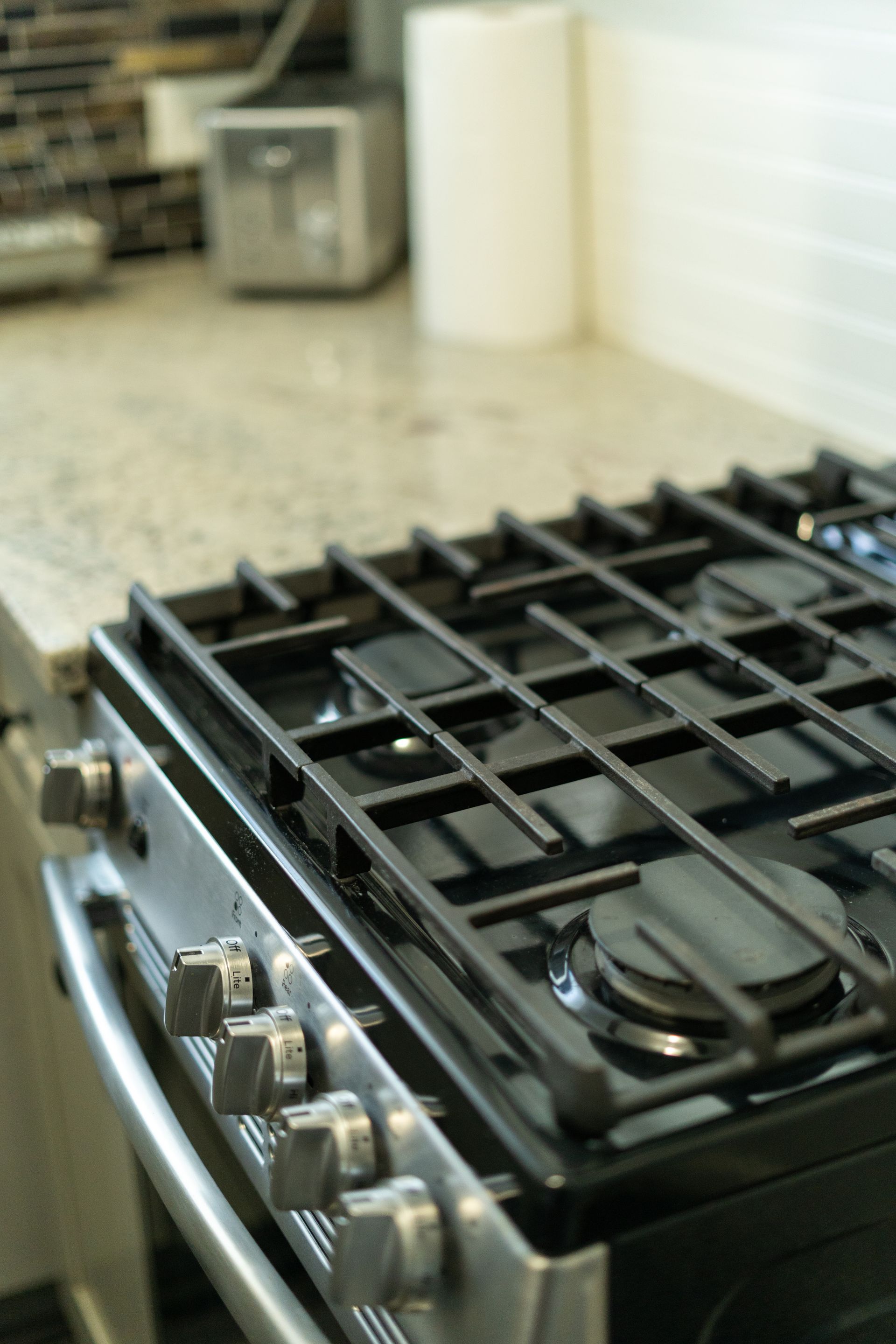 Close-up of a stainless steel gas stovetop with black grates and knobs on a kitchen countertop.
