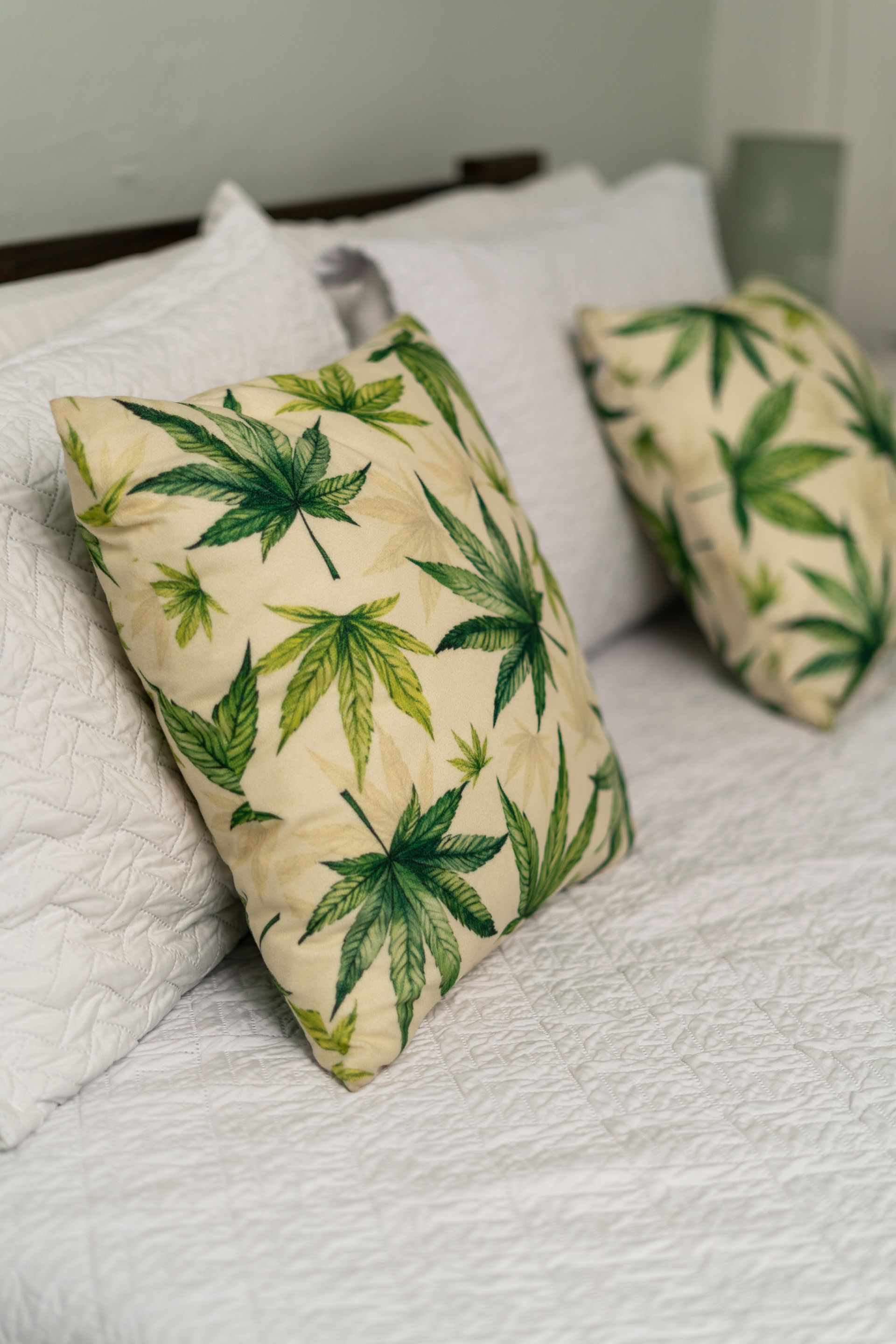 Bed with white pillows; cannabis leaf pattern pillows are in focus.