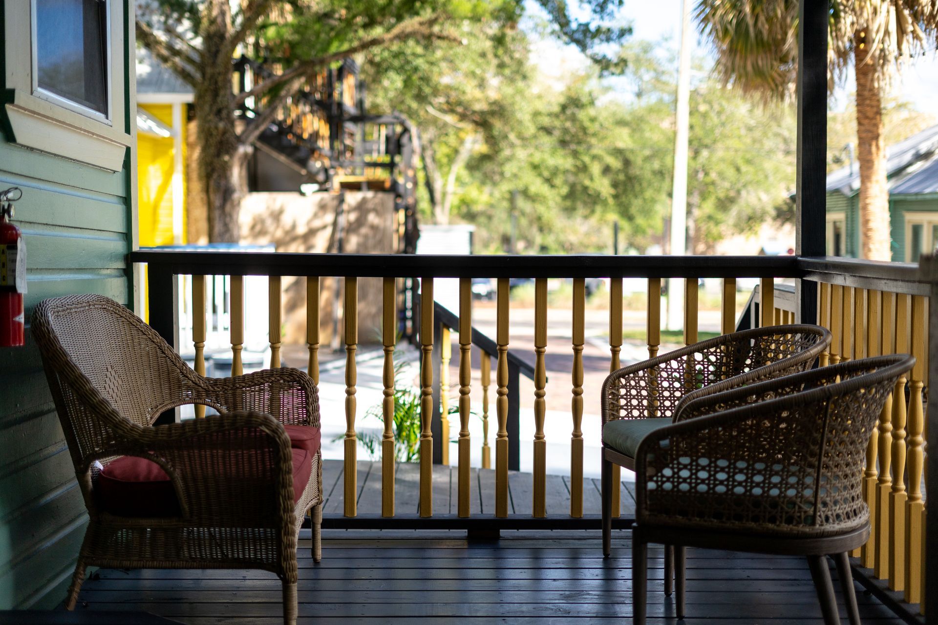 Porch with wicker chairs and railing, overlooking a street with trees and buildings.