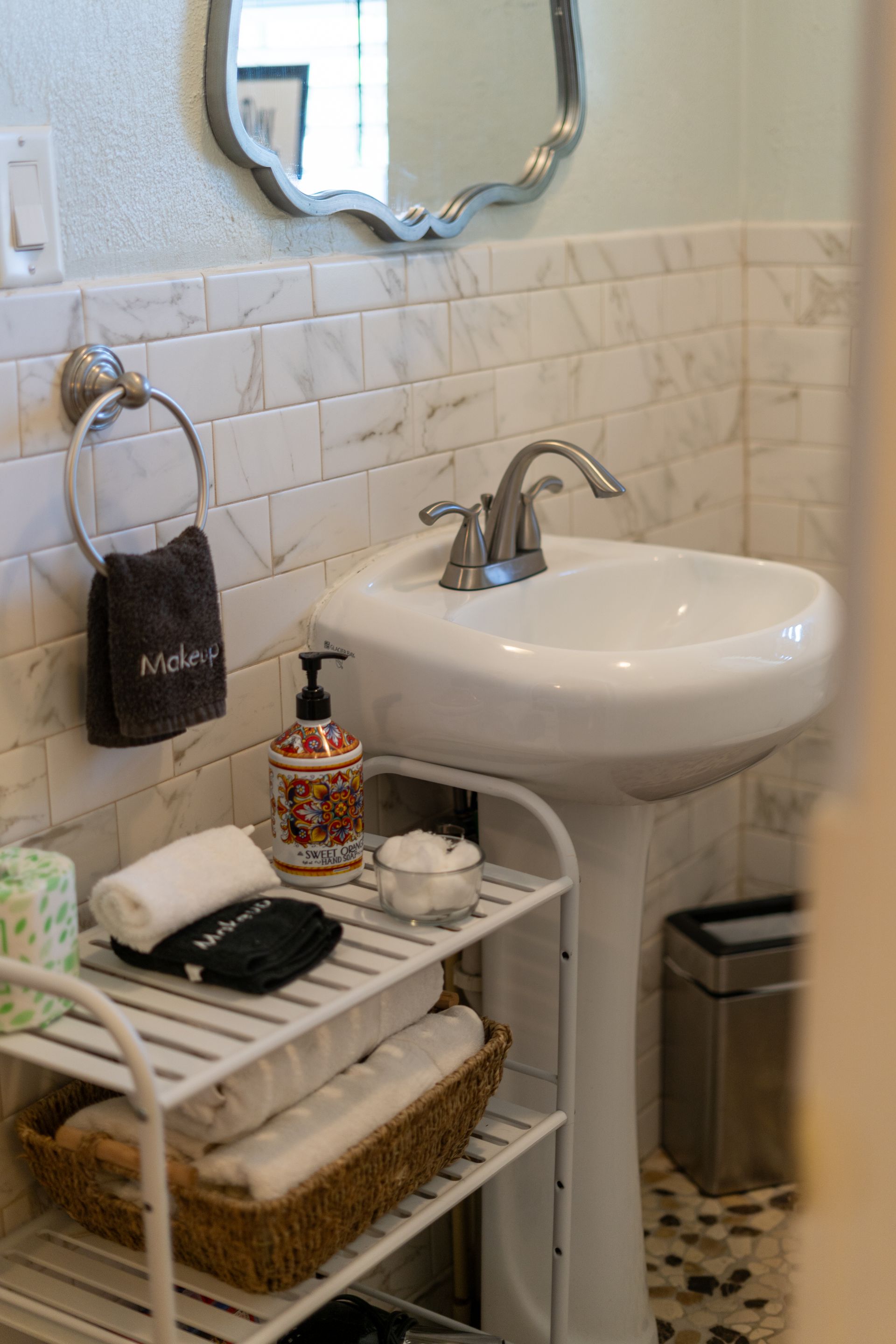 Bathroom with pedestal sink, white shelving with towels, hand towel holder, mirror.