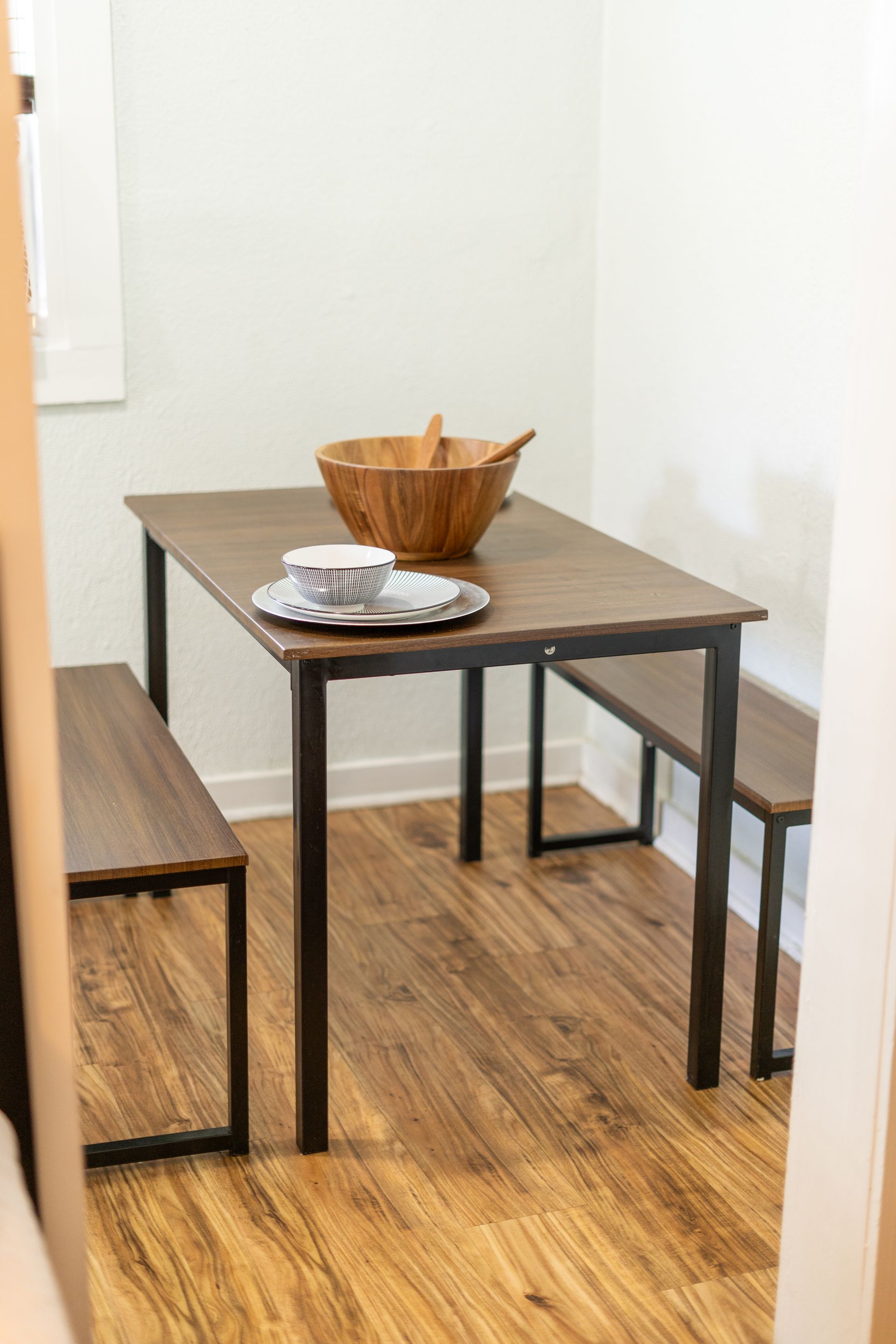 Dining table with two benches in a small room. Wooden bowl and plate on table.