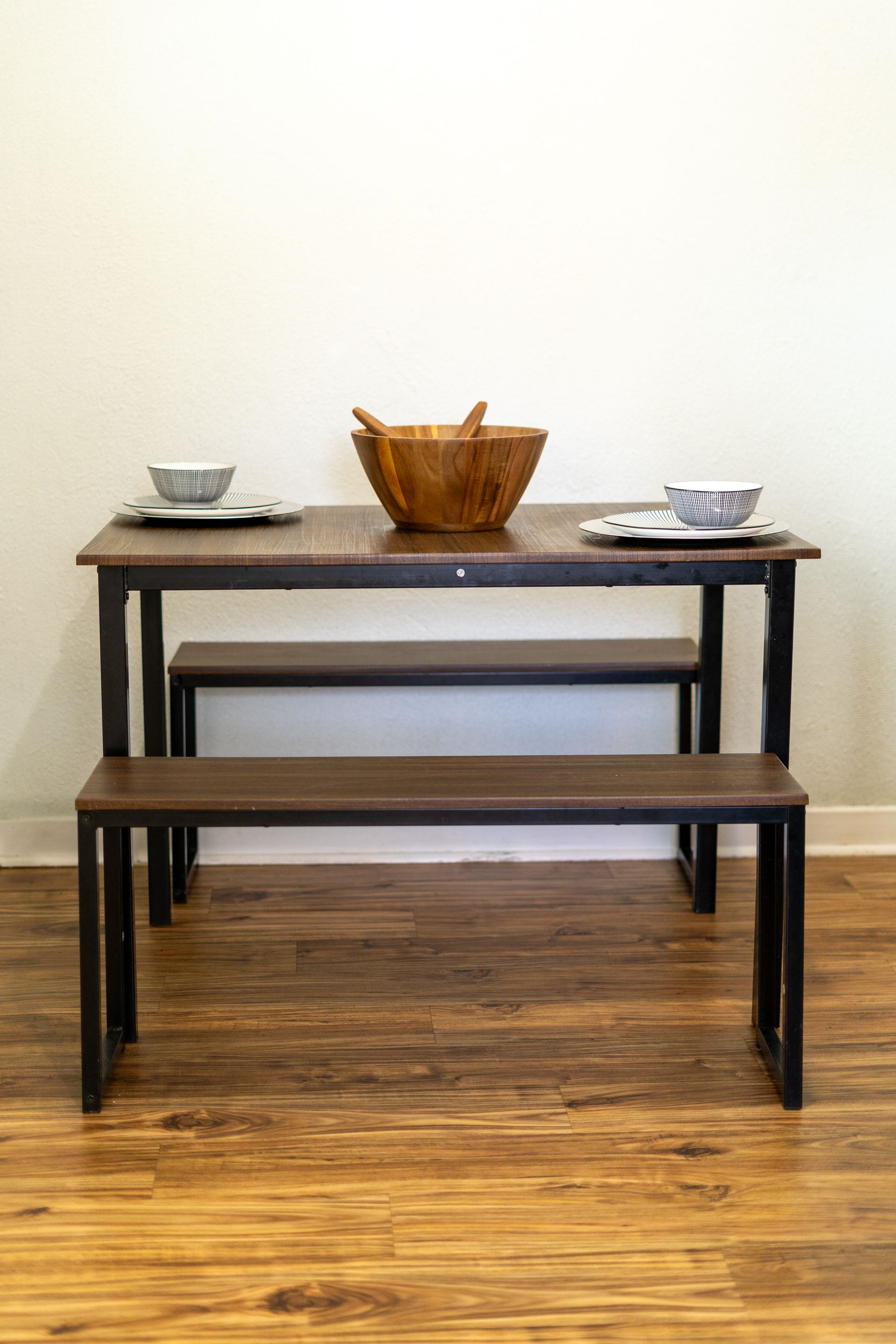 Wooden dining table with two benches, set with bowls and a salad bowl on a hardwood floor.